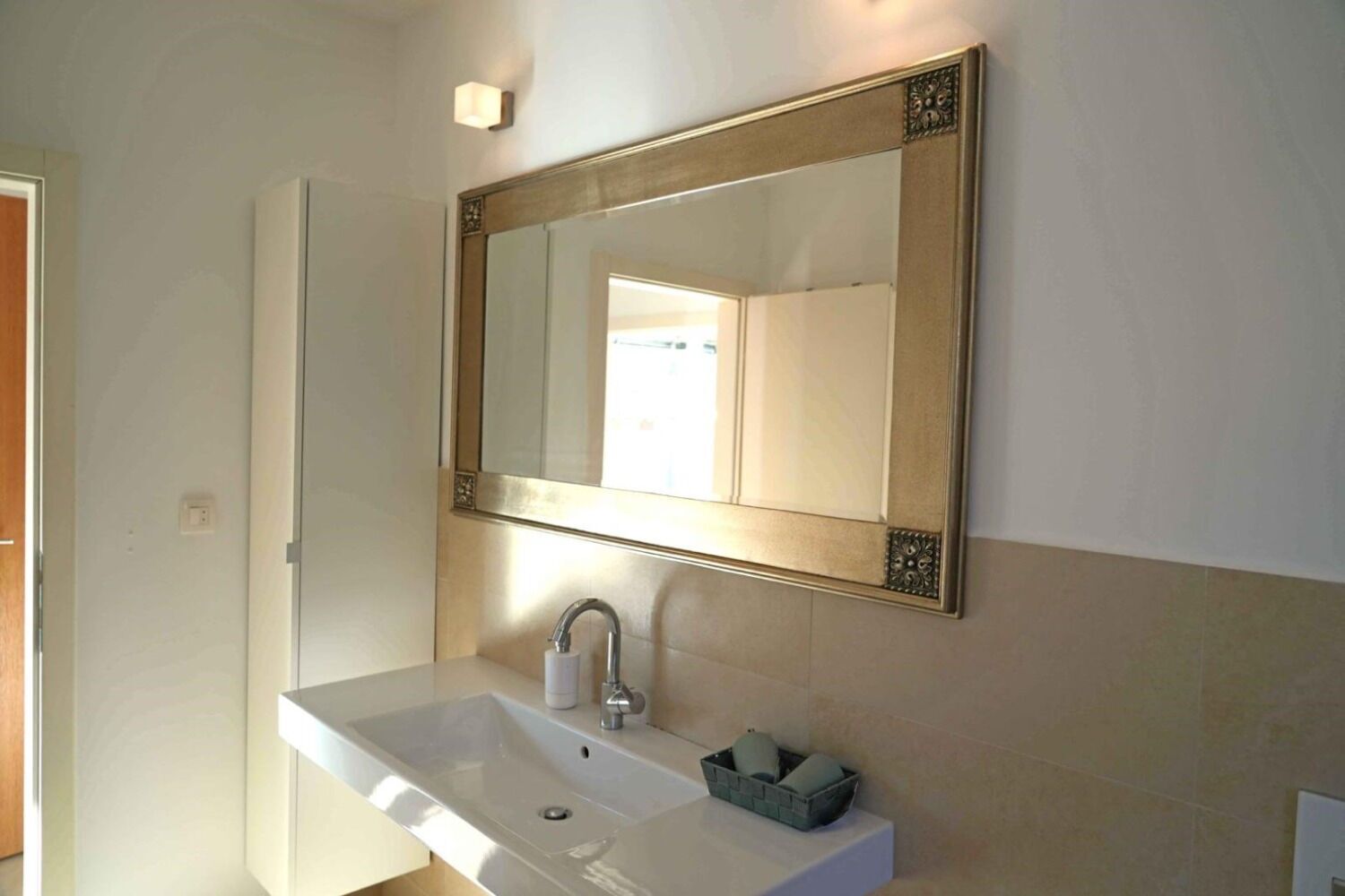 A bathroom with a white sink, a mirror with an ornate frame, and a towel rack with a basket.