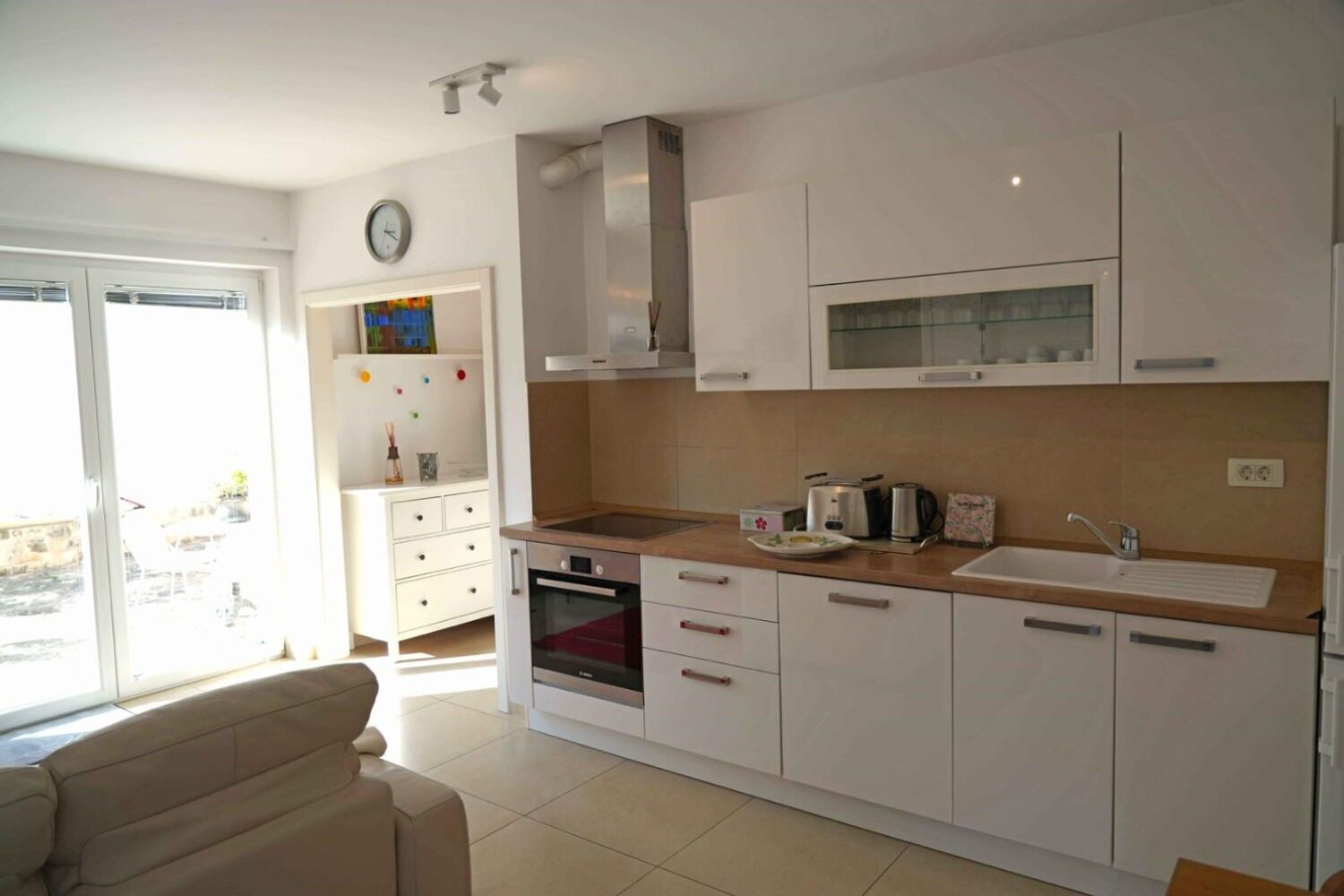 A modern kitchen with white cabinets, a built-in oven, a microwave, and a sink.