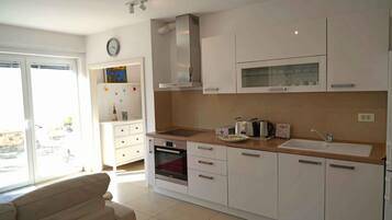 A modern kitchen with white cabinets, a built-in oven, a microwave, and a sink.