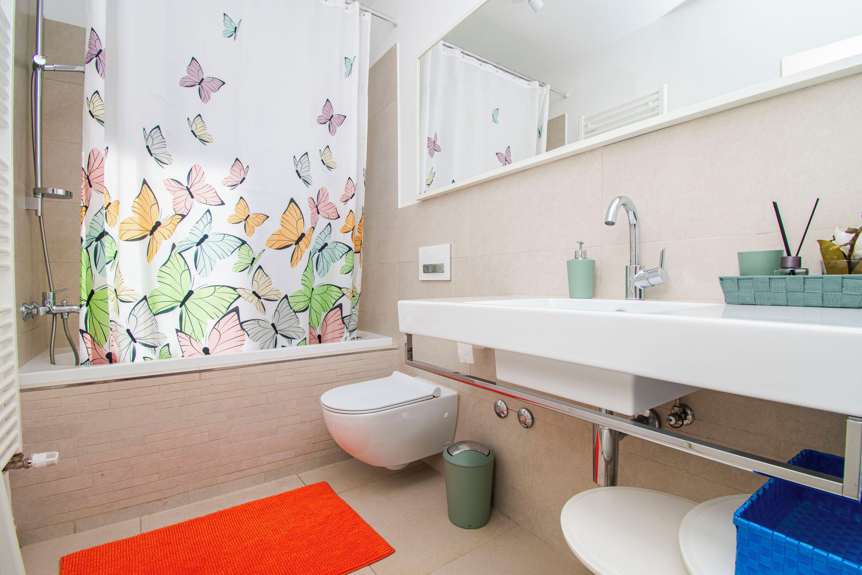 A bathroom with a shower, toilet, sink, and a trash bin.