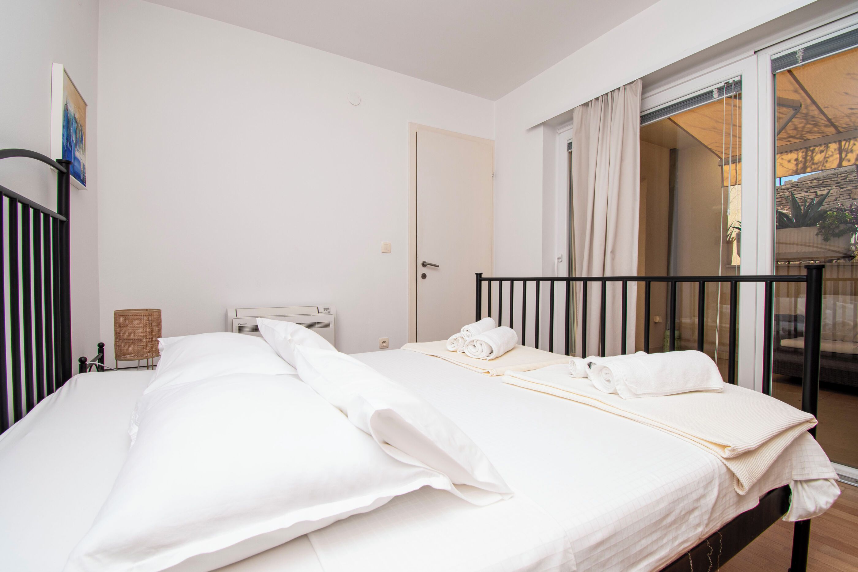 Habitación de hotel con cama, ventana con cortinas, puerta y una pequeña mesa con lámpara.