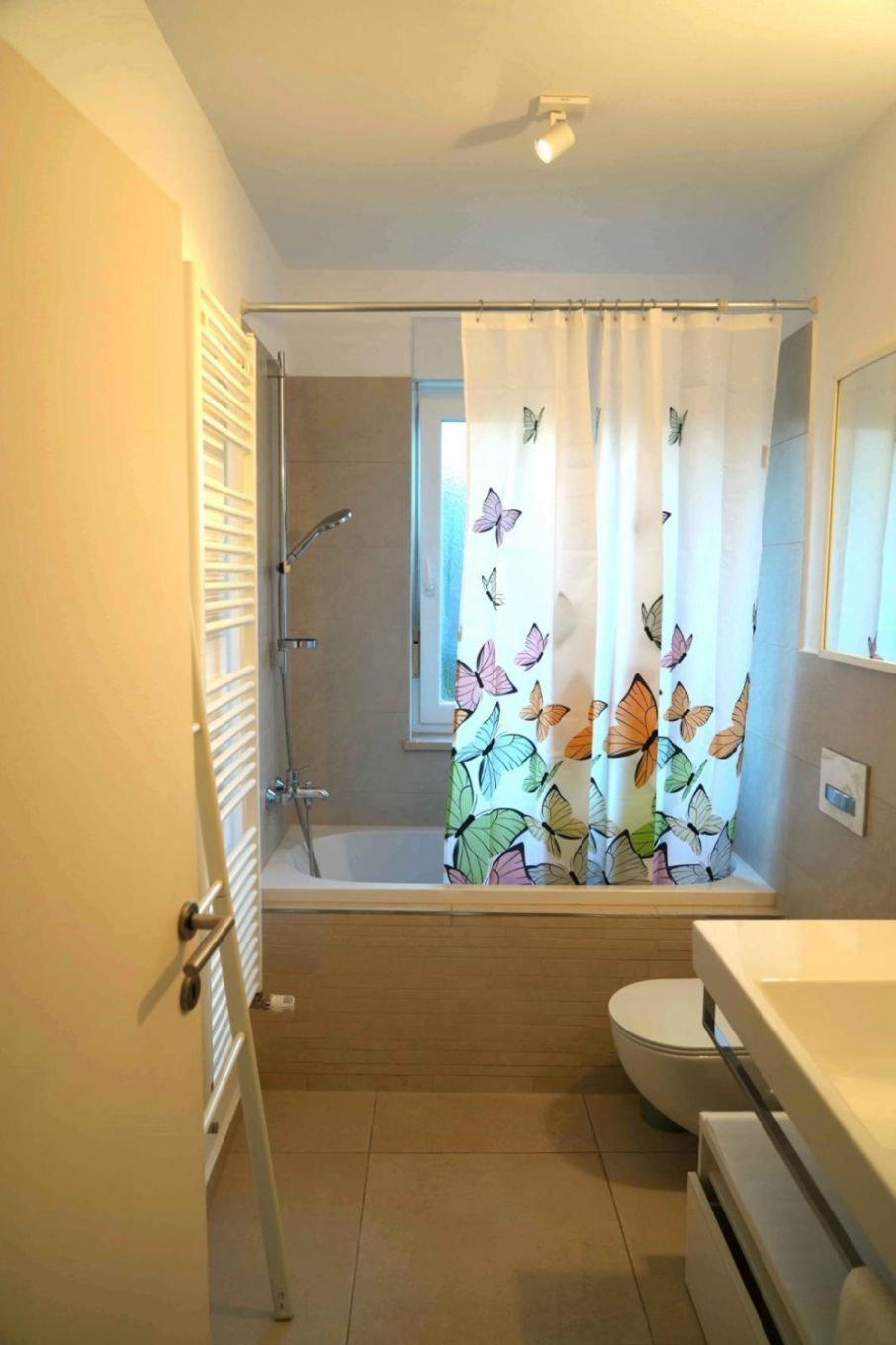 A bathroom with a shower, toilet, and a window with a butterfly curtain.