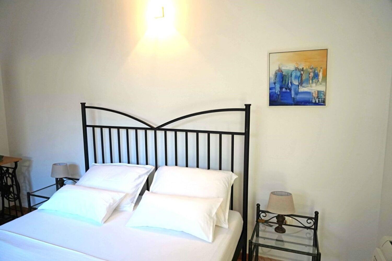 Un letto rifatto con lenzuola bianche, una testiera in metallo nero e un quadro appeso al muro.