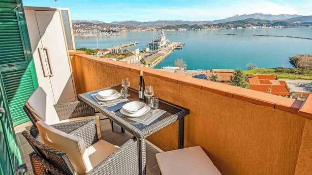 A balcony with a table set for two, overlooking a body of water and a harbor with ships. - La Scala Matta, Sea Lands (La Spezia)