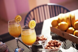 Två glas apelsinjuice står på ett bord tillsammans med en korg full med apelsiner och en skål med nötter.
