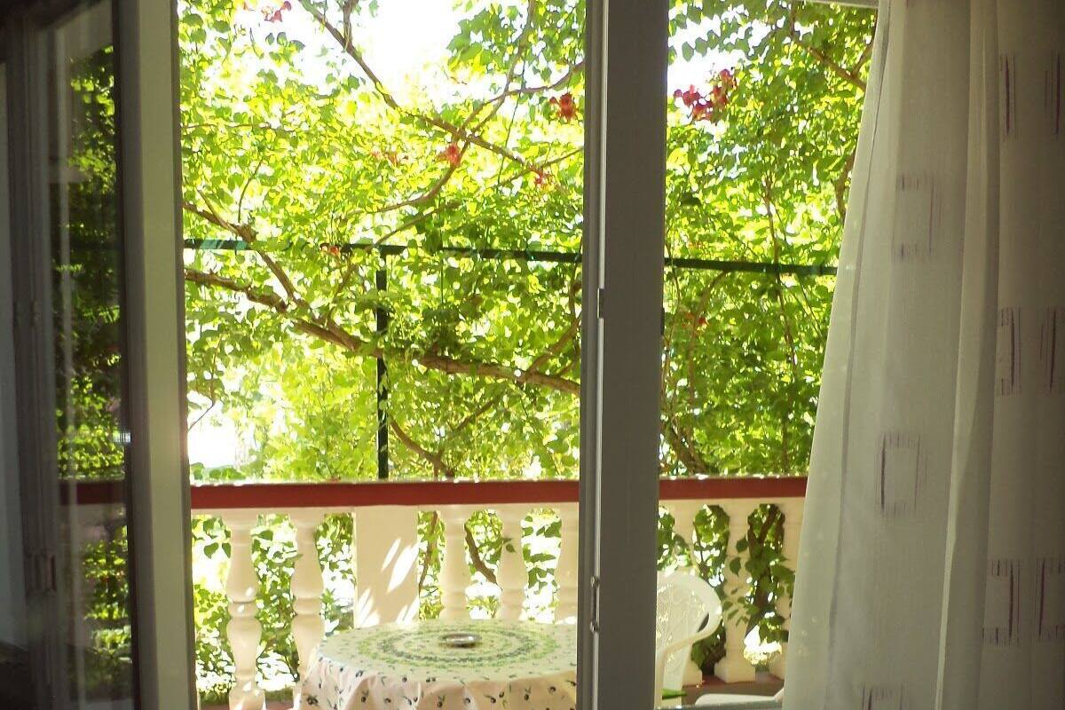 A room with a sliding glass door leading to an outdoor area with a table and chairs, a small garden, and a view of trees.