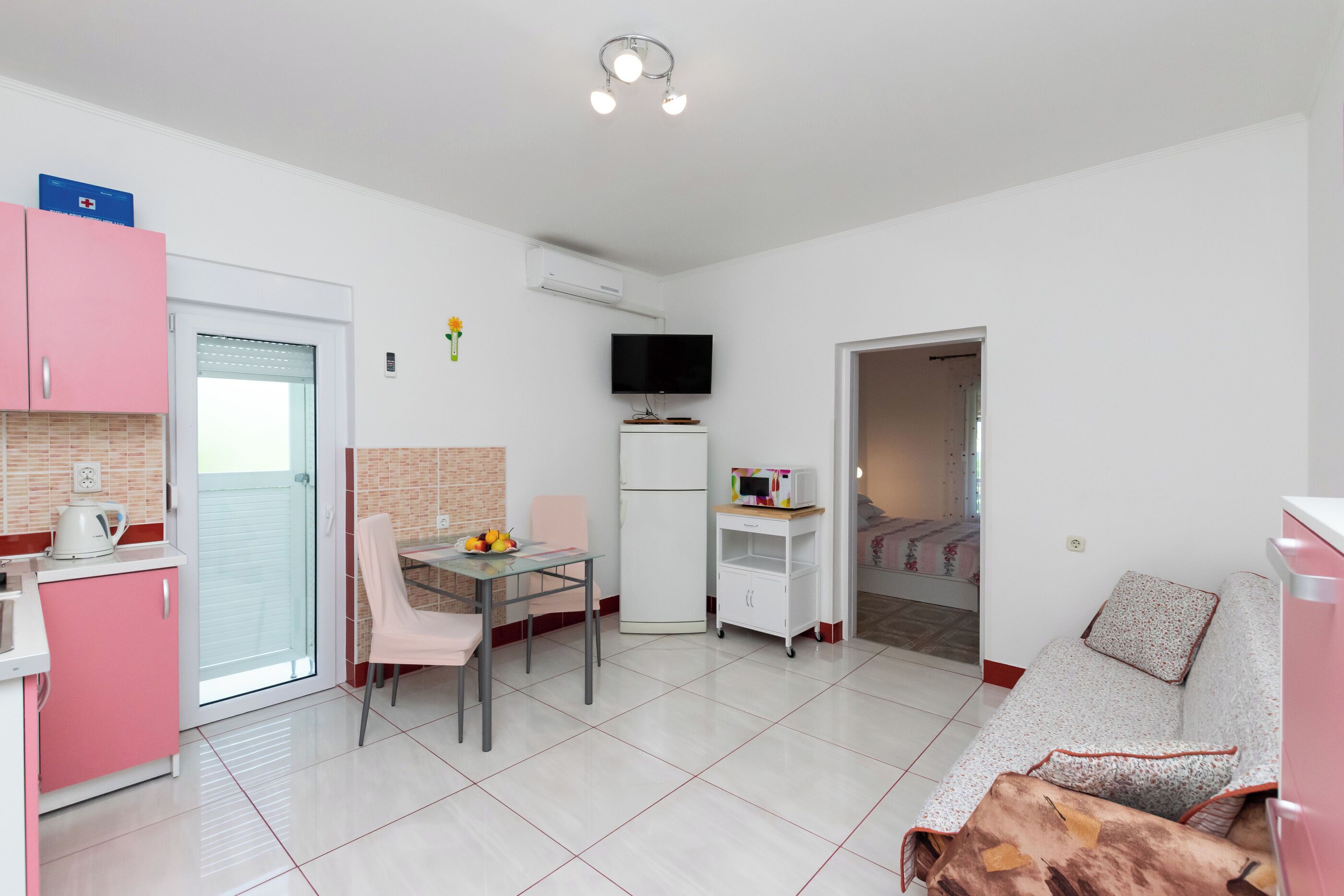 Un apartamento moderno con cocina, comedor y sala de estar. Incluye un televisor, refrigerador y un sofá.