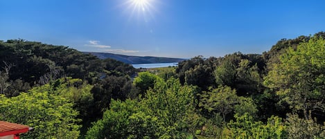 A view from a balcony with a red-tiled roof overlooking a lake and dense greenery.