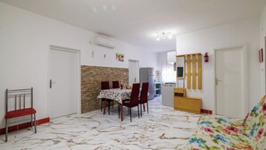 A dining area with a table set for four, a red chair, and a sofa with a floral pattern. - Apartments Grga (Lopar)