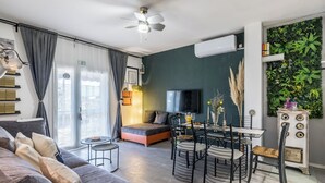 A modern living room with a sofa, a dining table with chairs, a TV, and a ceiling fan. - Apartments Holiday Home Book (Opuzen)