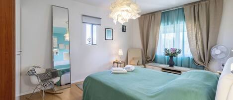 A bedroom with a green bedspread, a rocking chair, a bedside table with a lamp, and a large mirror.