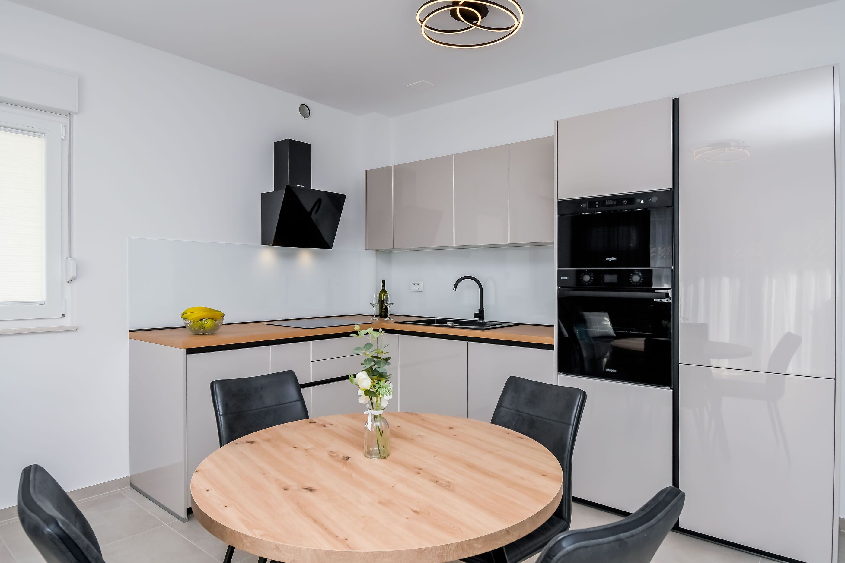 A modern kitchen with a round wooden table, black chairs, and a built-in oven.