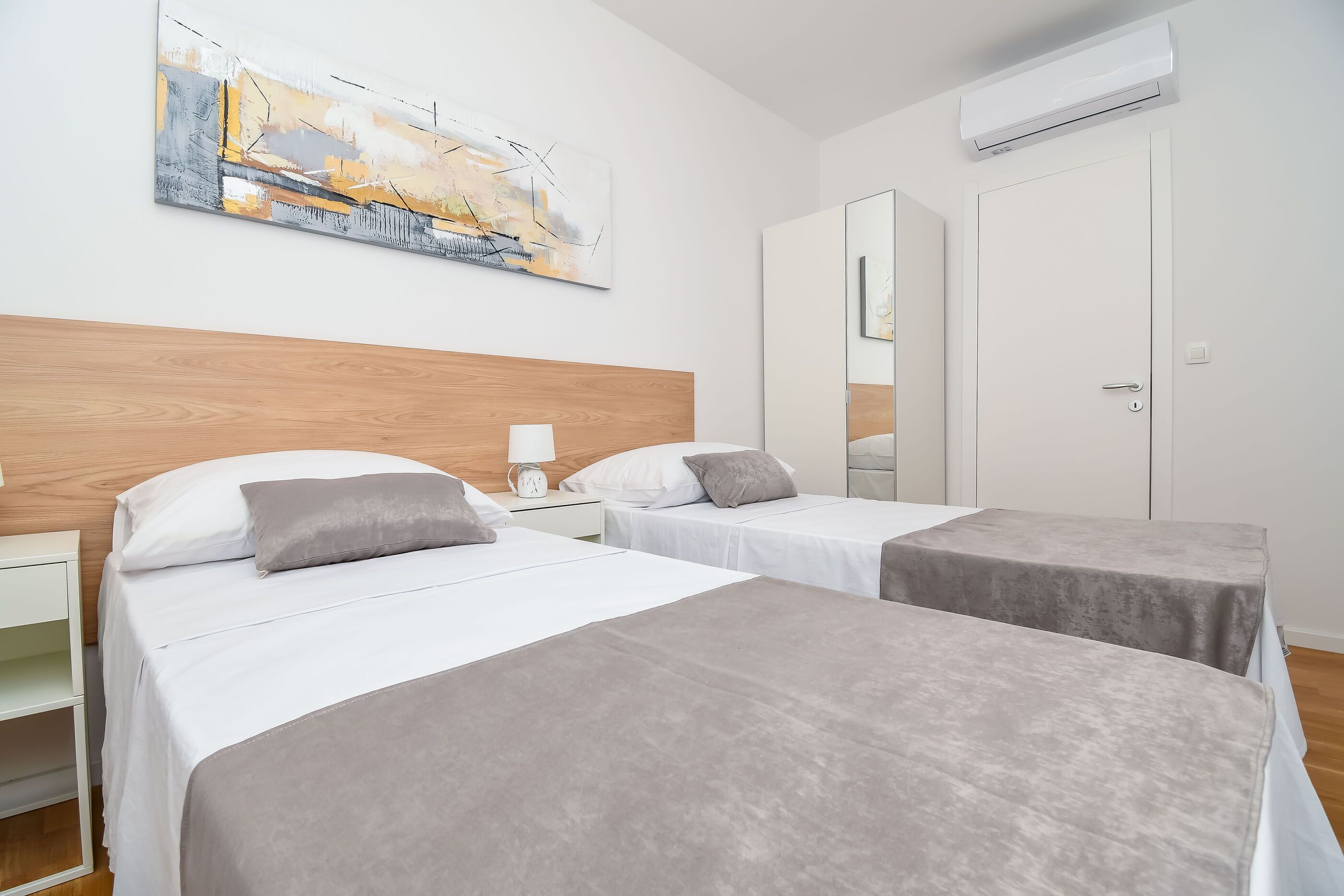 Et hotelværelse med to senge, et træsengegærde, et billede på væggen og en aircondition.