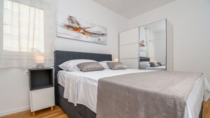 Une chambre à coucher moderne avec un lit, des tables de chevet, un grand miroir et une œuvre d’art murale.
