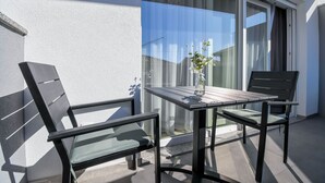 Un balcon avec une table et deux chaises, un vase rempli de fleurs et une vue sur le ciel et les bâtiments.