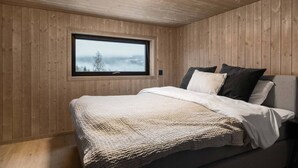 A bedroom with a wooden paneled wall, a large window, a bed with pillows, and a ceiling light. - Trysil Ski-in/out Apt, newly built (Trysil)