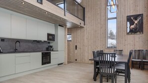 A modern kitchen with white cabinets, a dining area with wooden chairs, and a large window with a view of trees. - Trysil Ski-in/out Apt, newly built (Trysil)