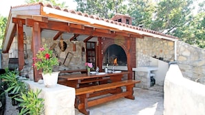 An outdoor patio with a stone wall, wooden pergola, and a brick fireplace. - House Anamaria (Posedarje)