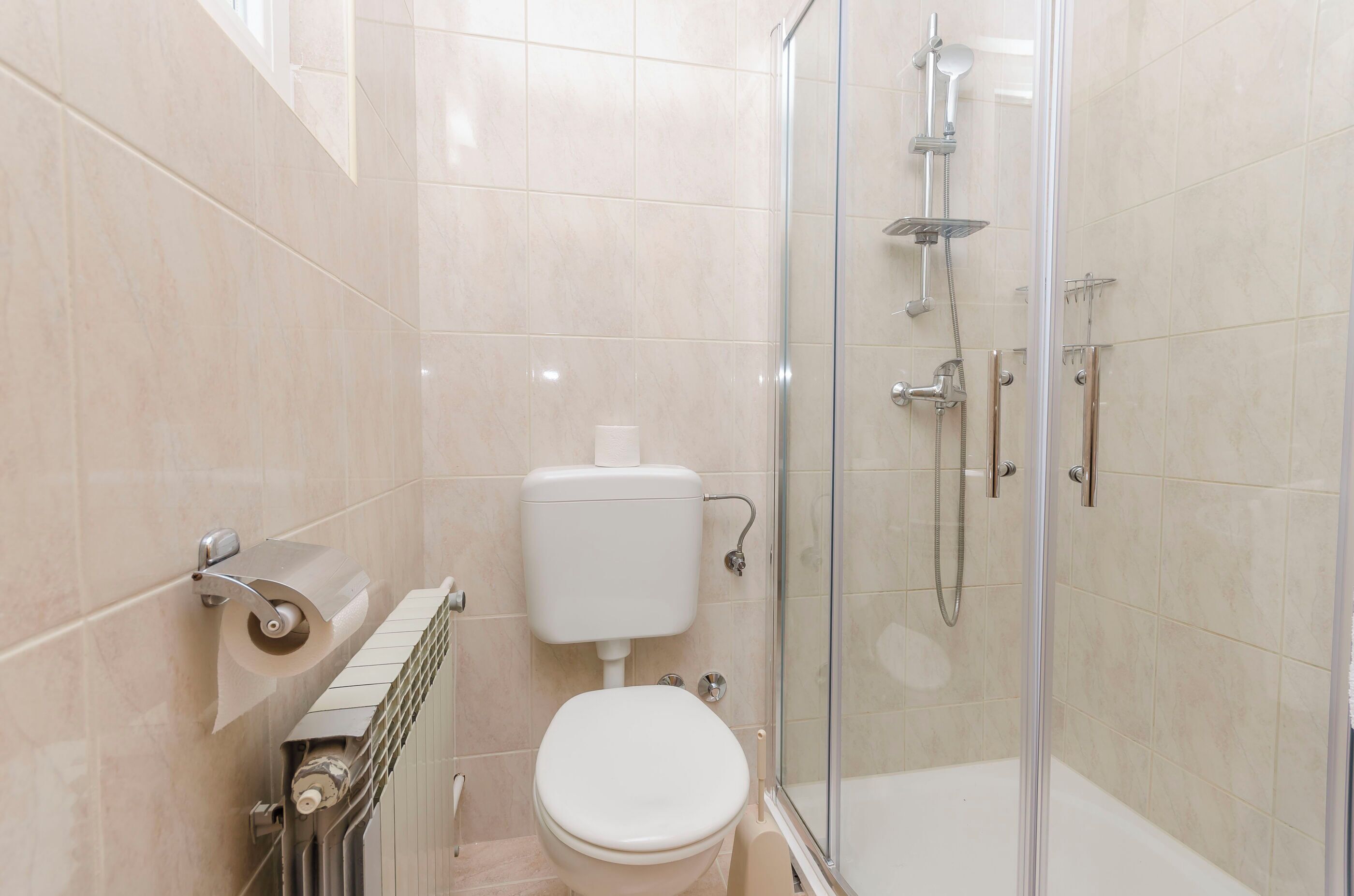 Moderni kylpyhuone, jossa on wc, lasiseinällä varustettu suihku ja wc-paperiteline.