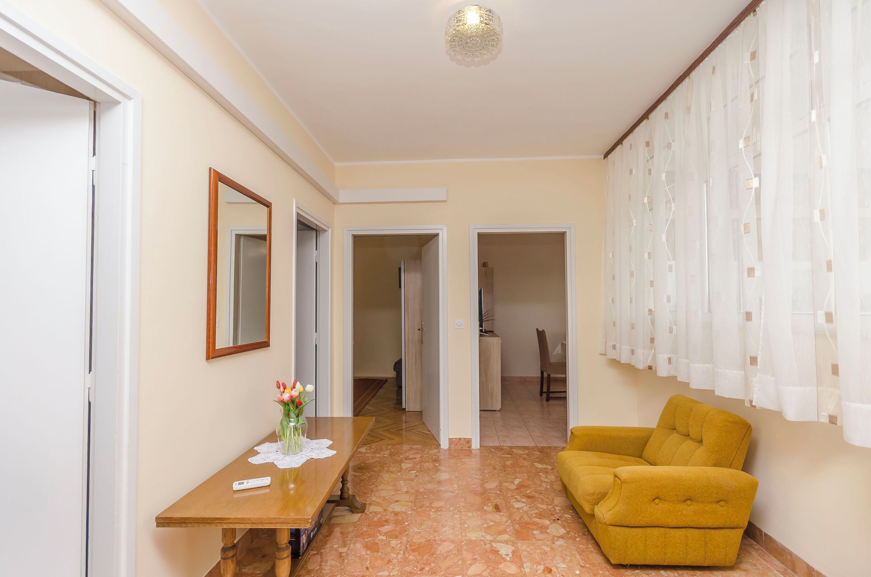 A room with a wooden table, a yellow armchair, a mirror, and a door leading to another room.