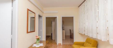 A room with a wooden table, a yellow armchair, a mirror, and a door leading to another room.