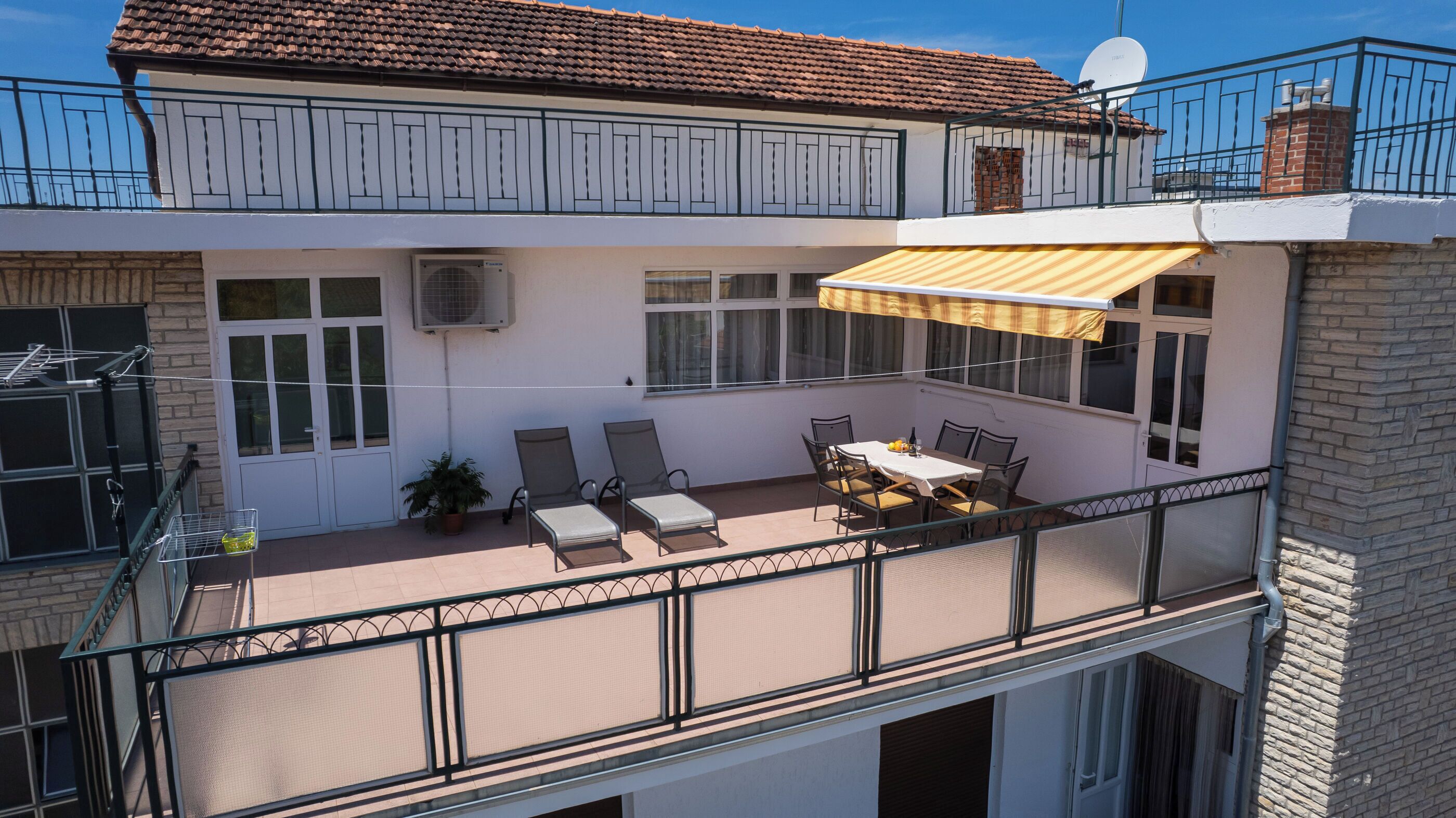 A two-story building with a balcony, a dining area with chairs and a table, and a satellite dish.