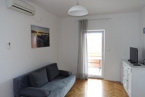 A modern living room with a grey sofa, a white cabinet with a TV, a ceiling fan, and a large window with curtains. - Apartments Lea Patrik Mara (Nin)