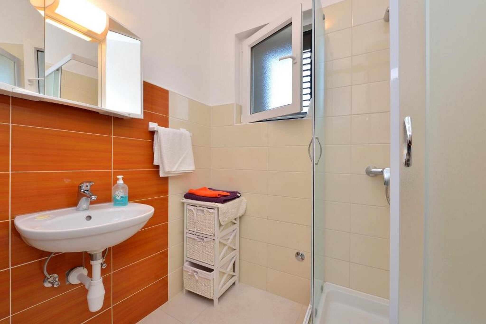 Casa de banho com lavatório branco, espelho, toalheiro, armário pequeno e área de duche.