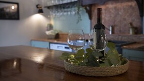 A bottle of wine and two glasses on a wooden table with a woven basket, surrounded by green leaves and small lights. - House Casa Huerta (Netretic)