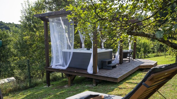 A wooden deck with a canopy bed, a hot tub, and lounge chairs. - House Casa Huerta (Netretic)