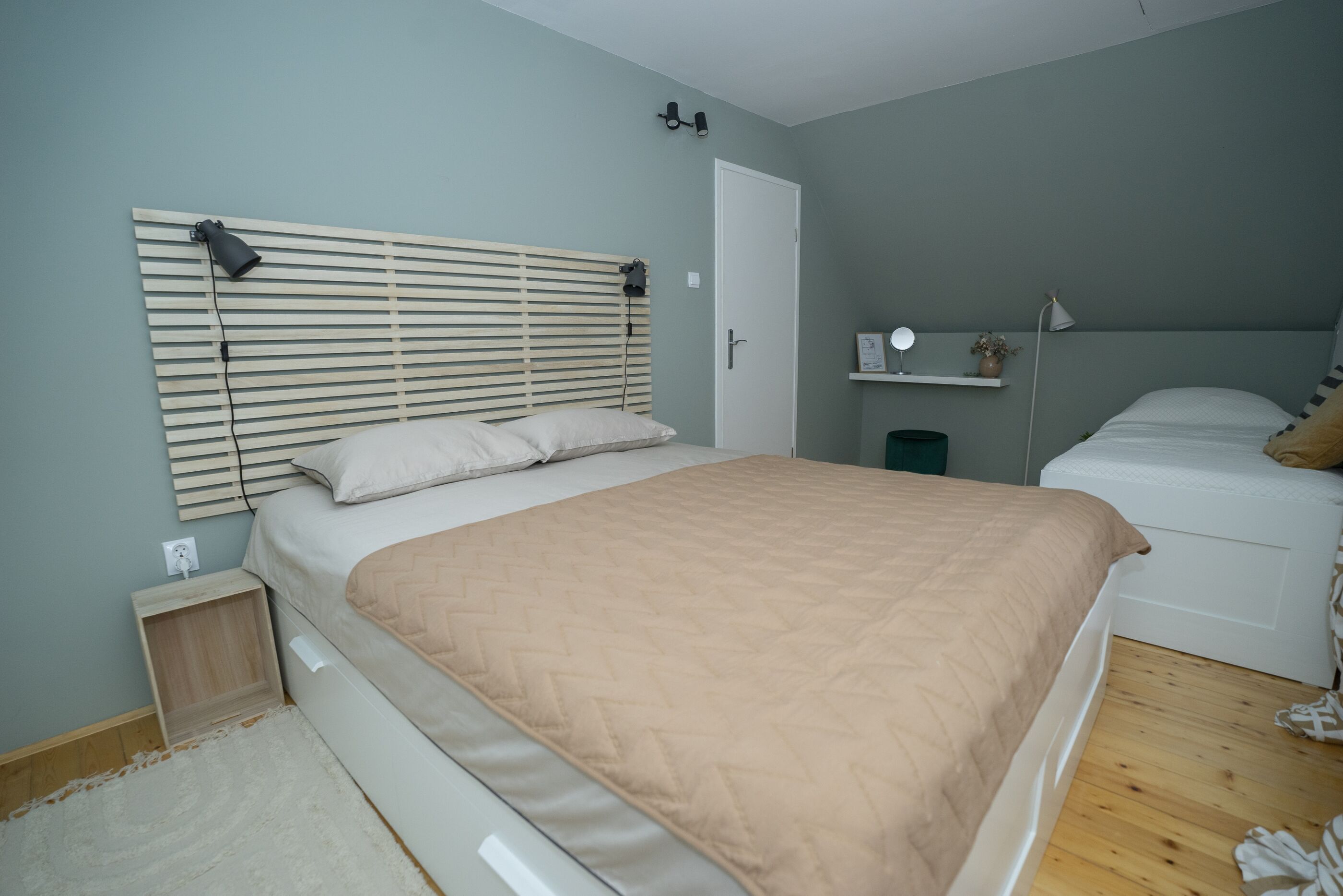 Ein Schlafzimmer mit Bett, Nachttisch, Lampe und einer kleinen Ablage mit einer Pflanze.