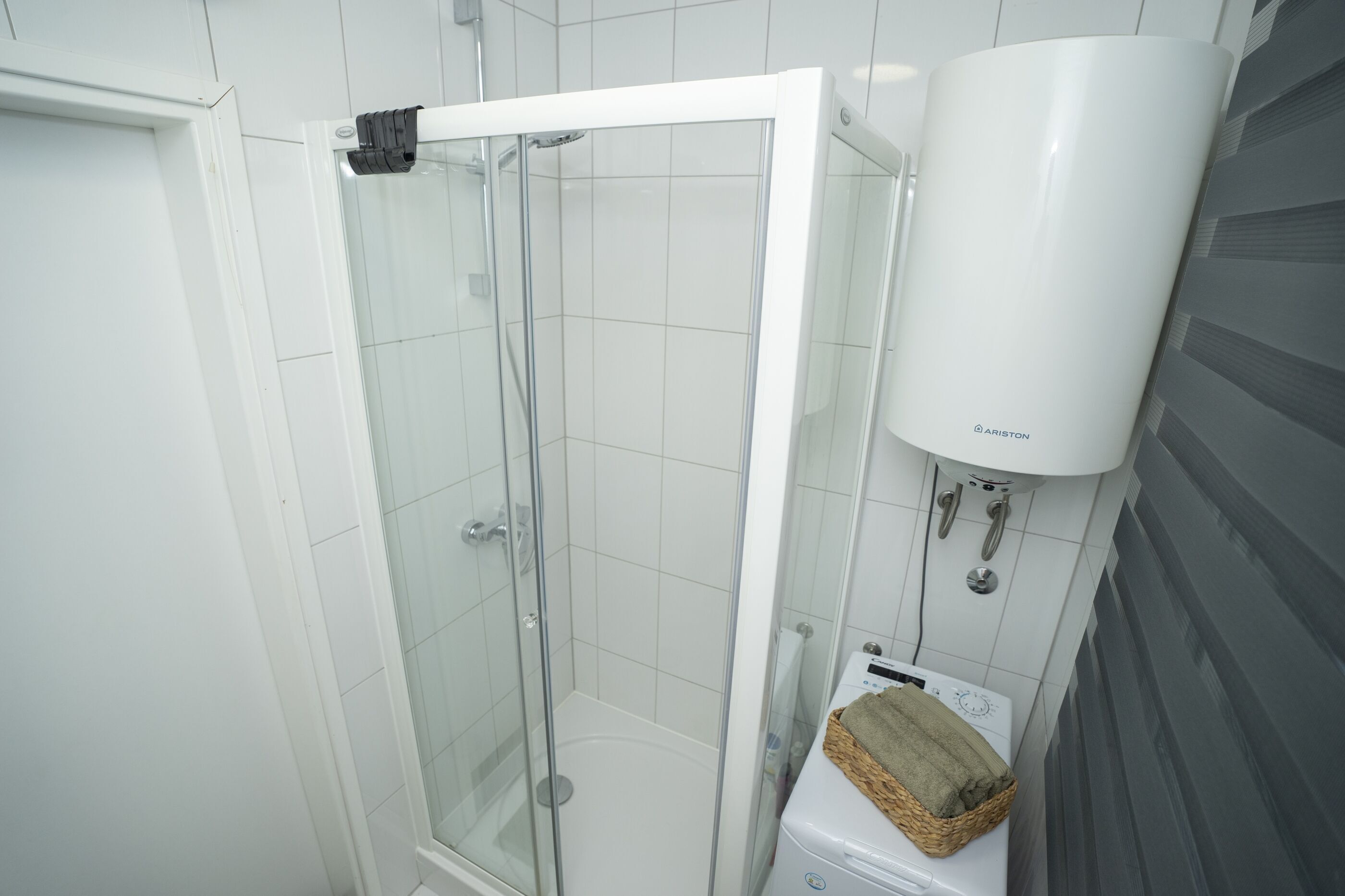 Box doccia con porta in vetro, un water bianco e un porta asciugamani con cesto.