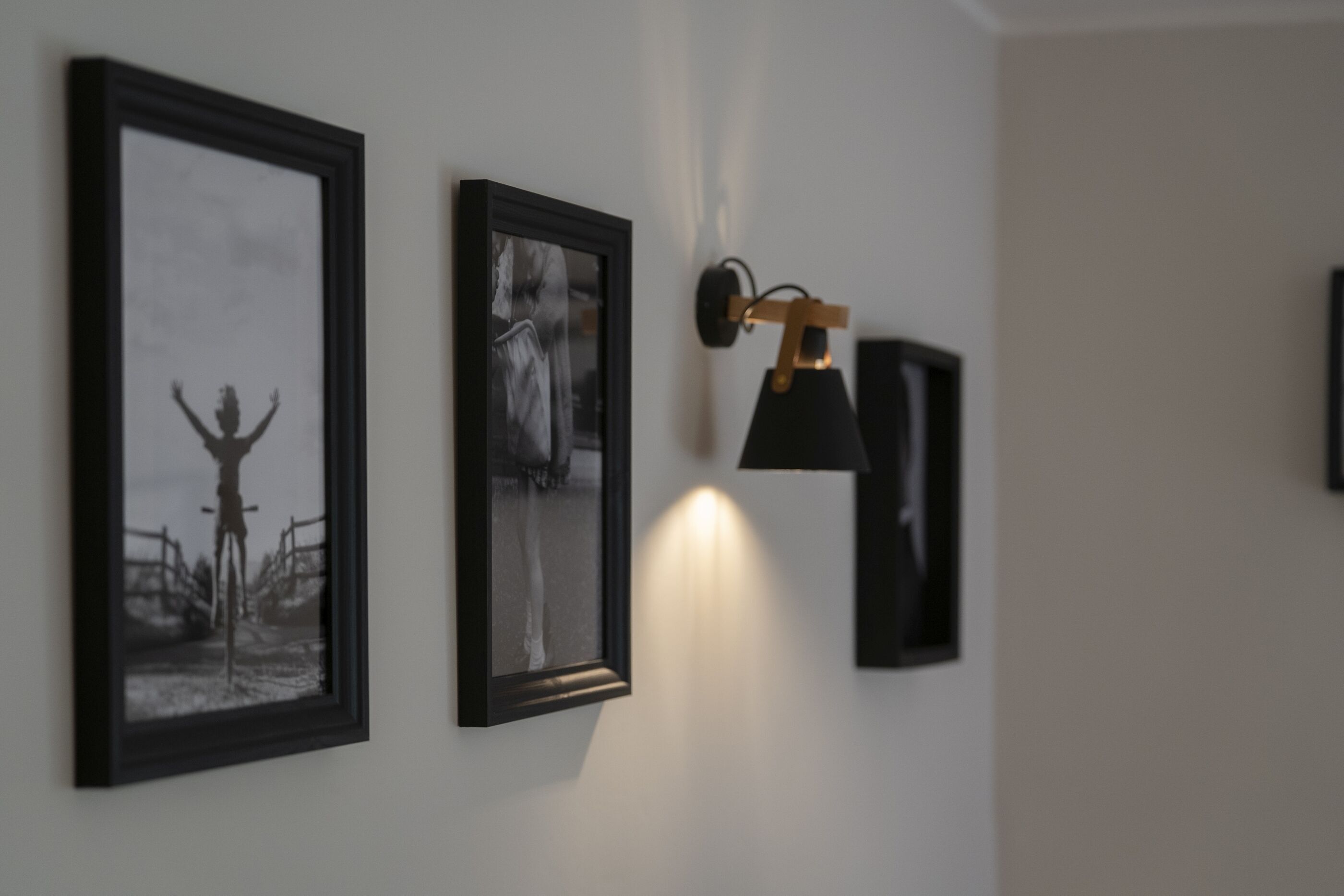 Un pasillo con fotografías enmarcadas en la pared y una lámpara fijada a la pared.
