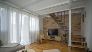 A modern living room with a brick wall, wooden staircase, and a flat-screen TV. - House Casa Huerta (Netretic)