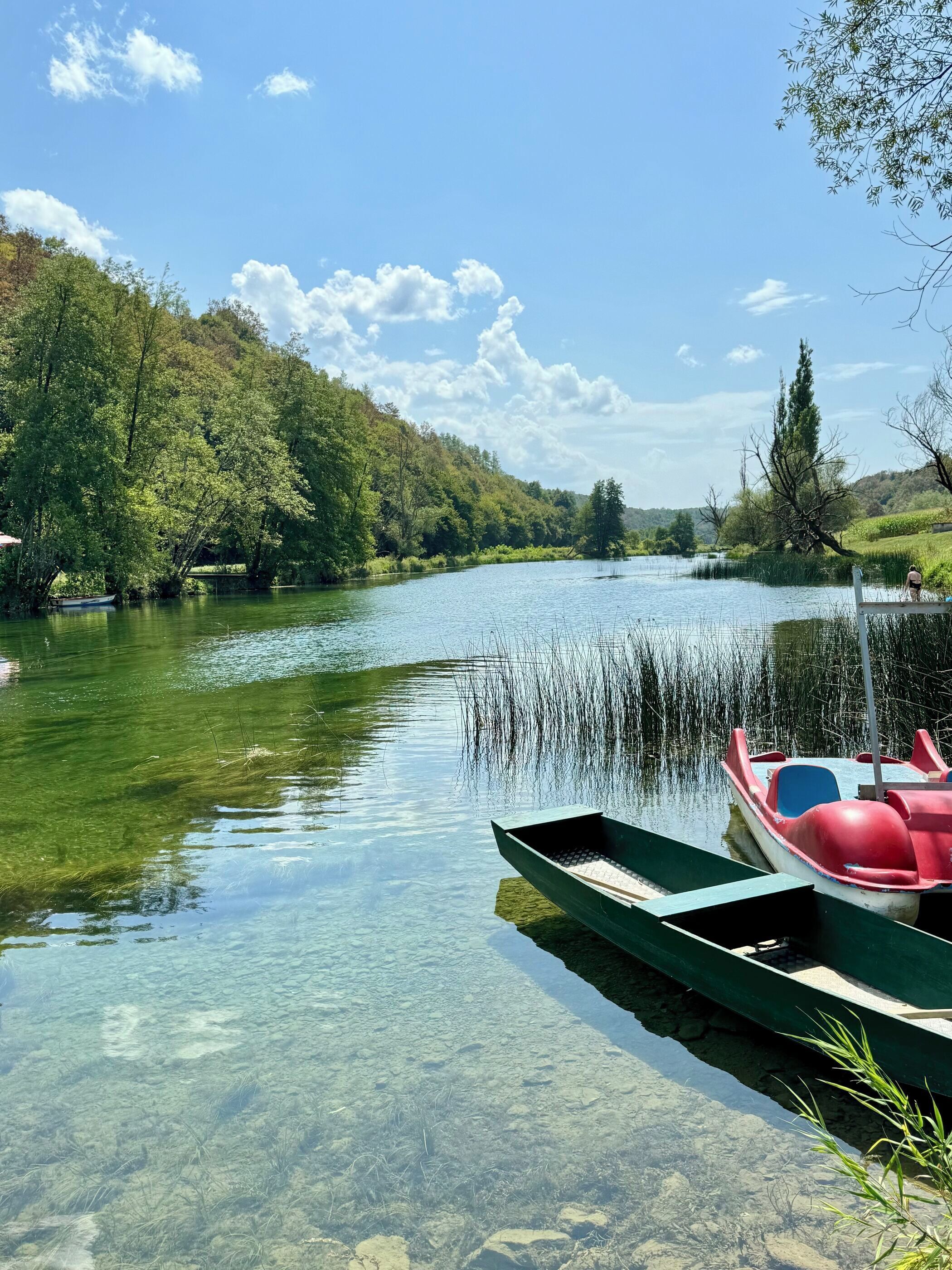 Un río tranquilo con barcos amarrados, rodeado de exuberante vegetación y cielos despejados.