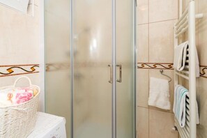 A bathroom with a glass shower door, a towel rack with towels, and a wicker basket with toiletries. - Apartment Zeljka (Dugi Rat)