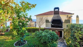 Una casa con zona de barbacoa, rodeada de vegetación y vistas al mar.