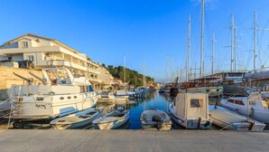A marina with various boats docked, a building with balconies, and a clear blue sky. - Apartment Zeljka (Dugi Rat)