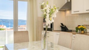 A modern kitchen with a marble countertop, a vase of white flowers, and a view of the sea through large windows. - Apartment Zeljka (Dugi Rat)