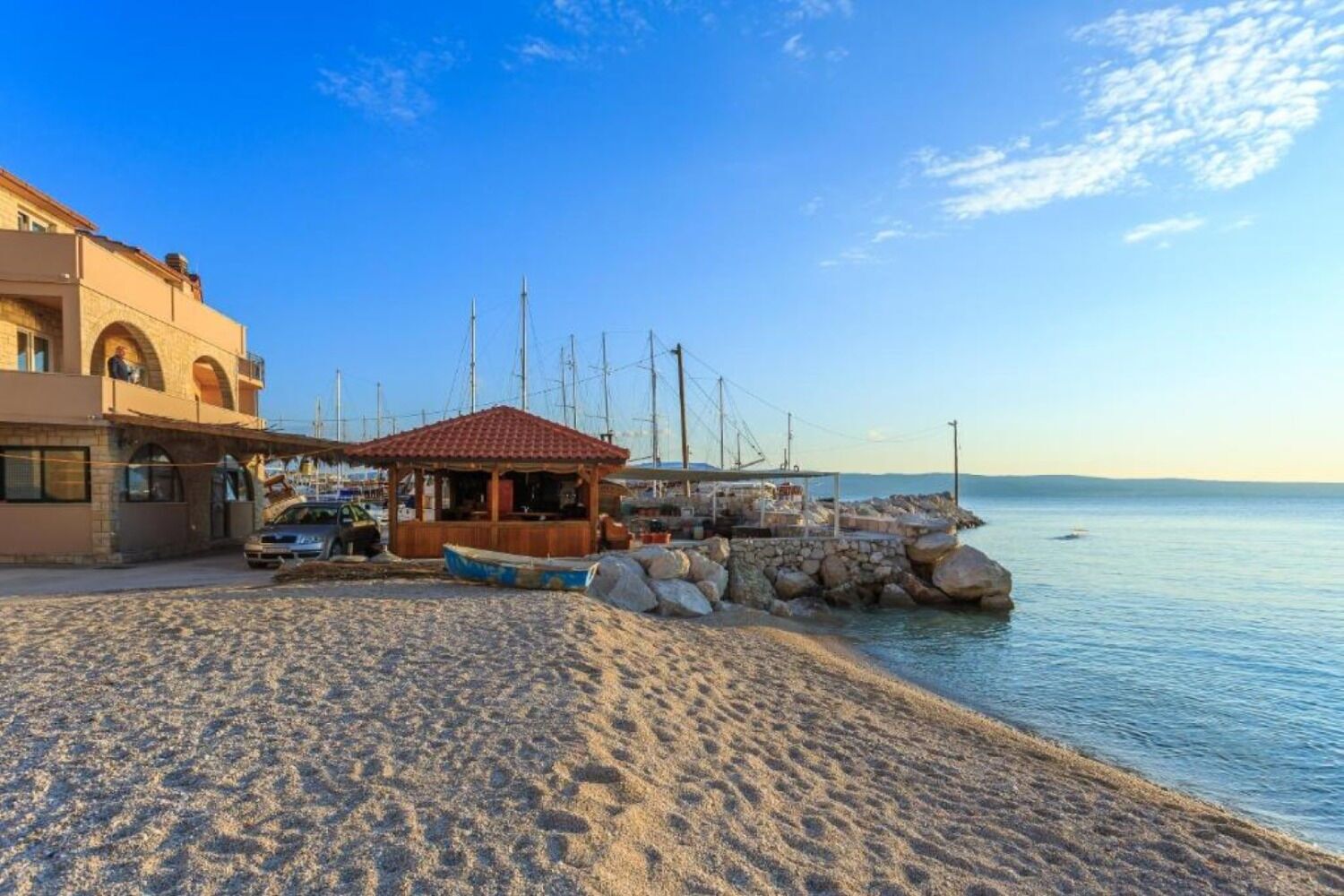 A coastal building with a tiled roof, a sandy beach, and a small wooden structure near the water.