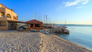 A coastal building with a tiled roof, a sandy beach, and a small wooden structure near the water. - Apartment Zeljka (Dugi Rat)