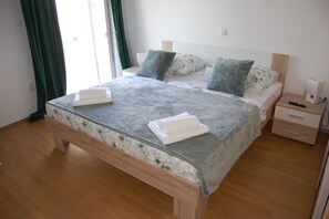Ein ordentlich bezogenes Bett mit einer blumigen Tagesdecke und zwei Kissen, ein Nachttisch aus Holz mit einer Lampe und ein Holzboden.