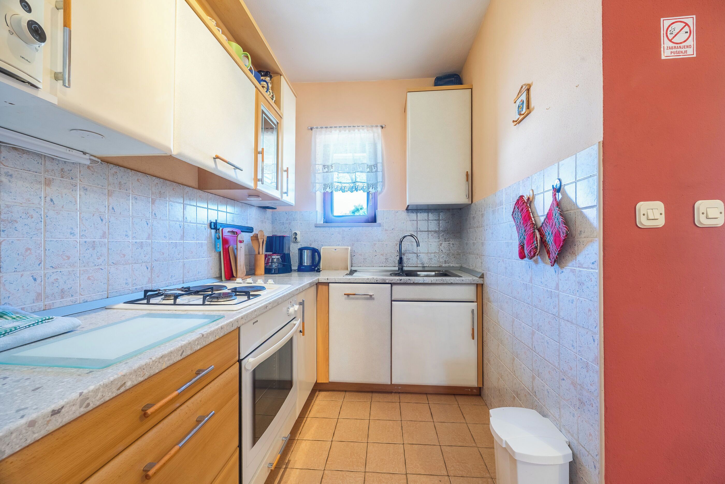 A compact kitchen with white cabinets, a gas stove, a sink, and a window with a curtain.