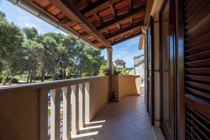 Ein Balkon mit Fliesenboden, Holzbalkon und Blick auf Bäume sowie ein Gebäude im Hintergrund.