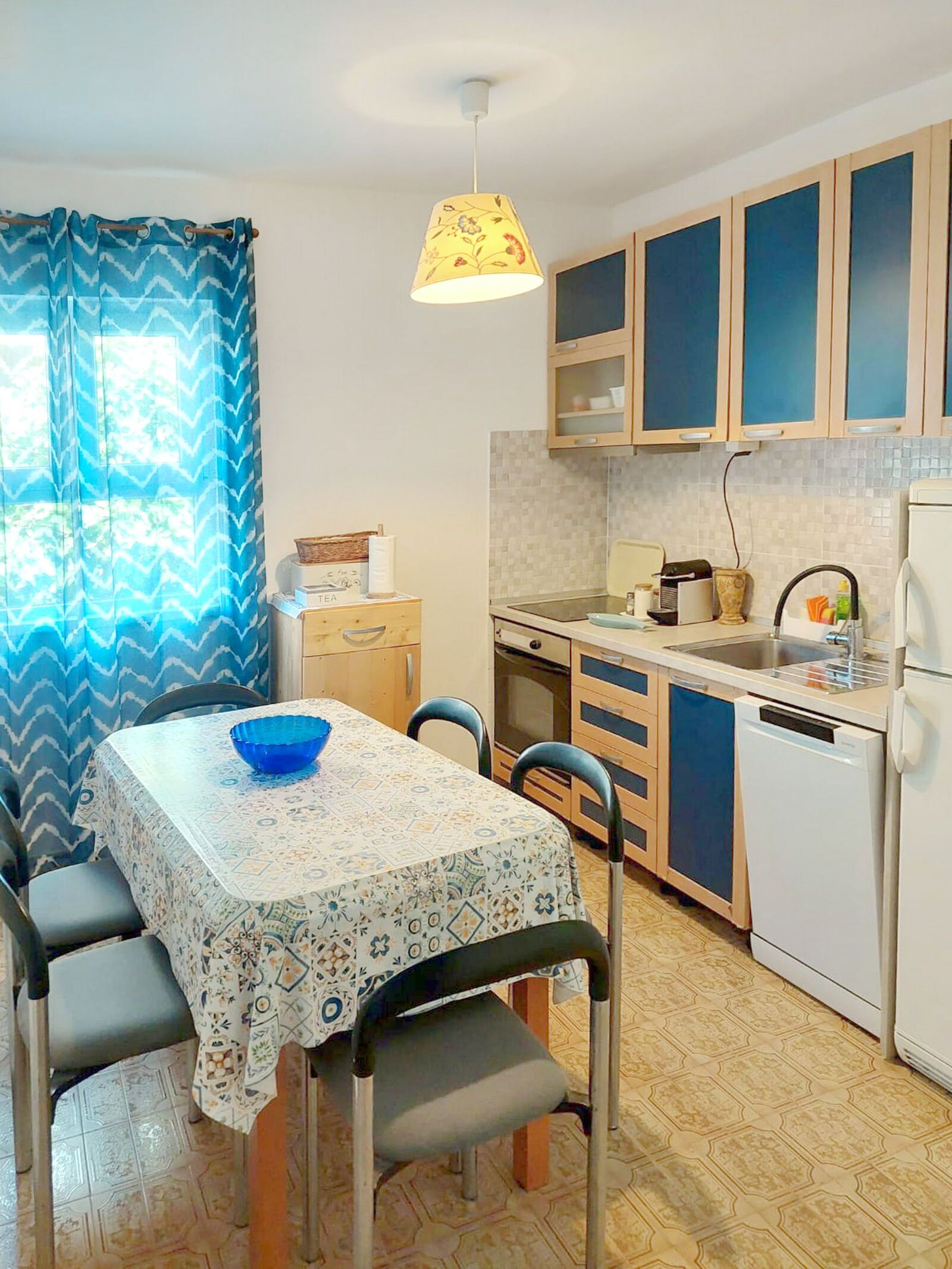 A compact kitchen with a dining table, chairs, a sink, and a refrigerator.