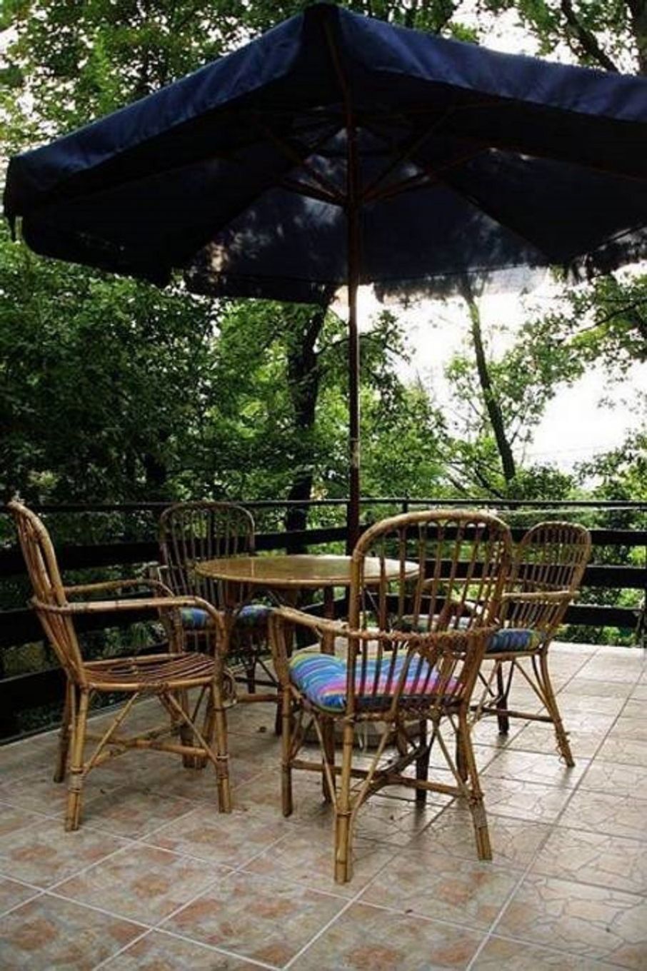 En udendørs patio med fletstole og et bord, overdækket af en stor parasol.