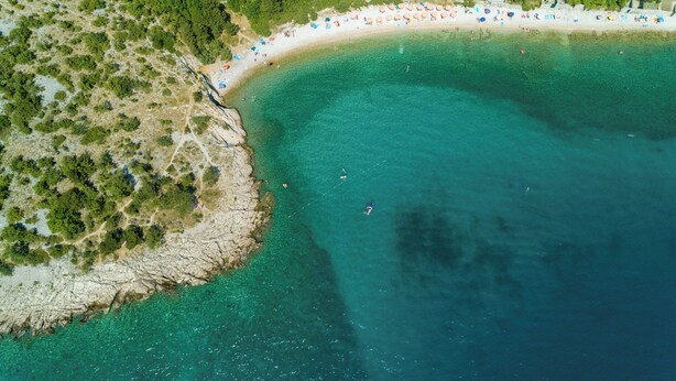 An aerial view of a beach with clear turquoise waters, a sandy shore, and a line of beach umbrellas. - Apartments Miro (Crikvenica)