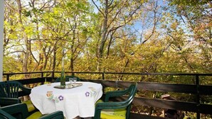 An outdoor patio with a round table and chairs, surrounded by a wooden railing and trees. - Apartments Miro (Crikvenica)