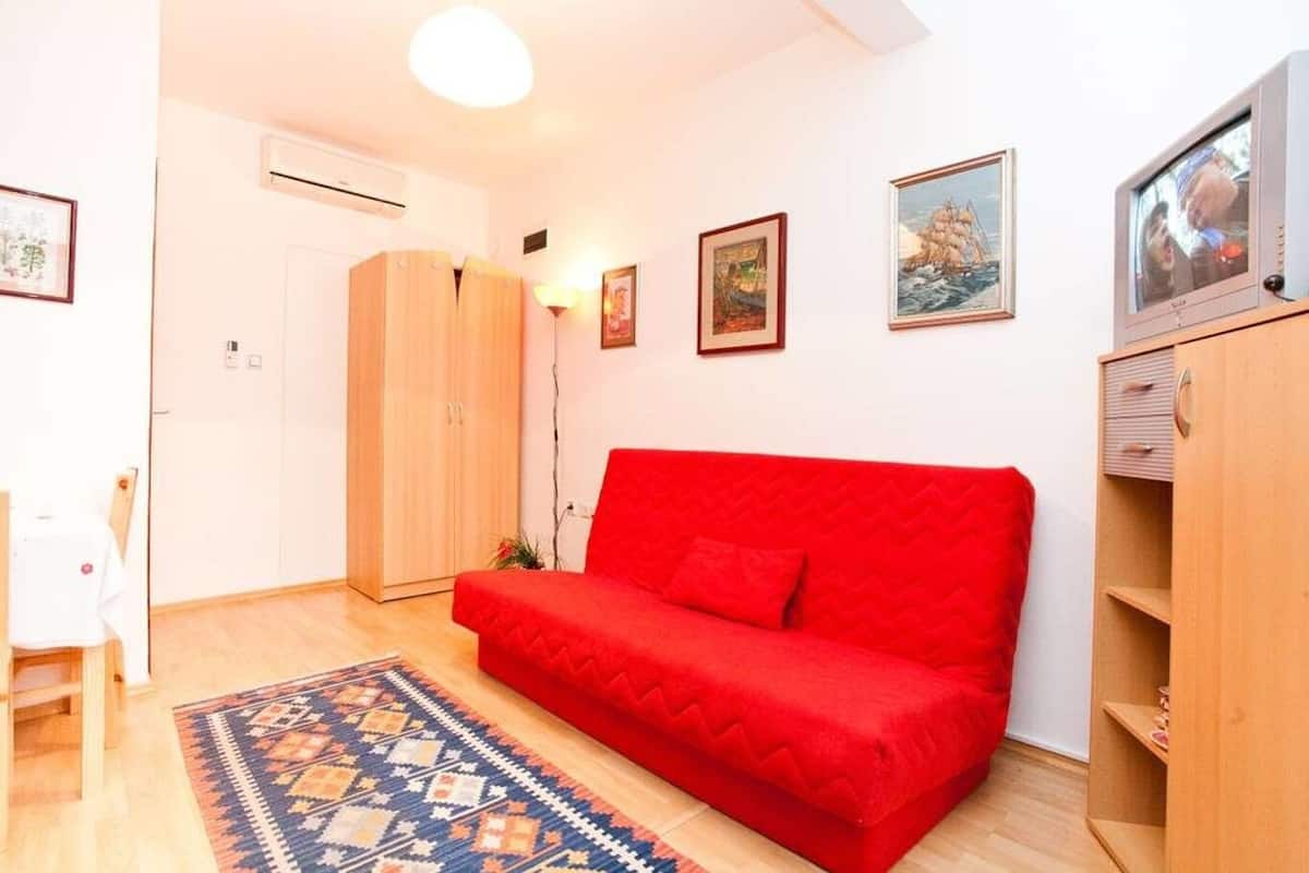 A small living room with a red sofa, a wooden wardrobe, and a television on a wooden stand.