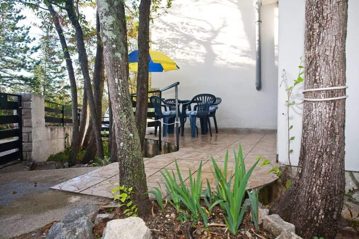 An outdoor patio with a table and chairs, surrounded by trees and a tiled floor.